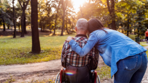 Image of a man in a wheelchair and a lady next to him with her arm around him